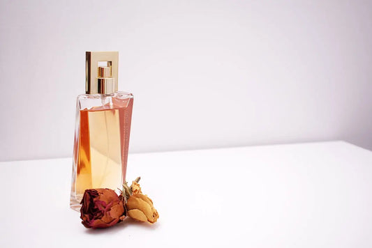 A shaped glass perfume bottle lies on the table with a rose decoration next to it