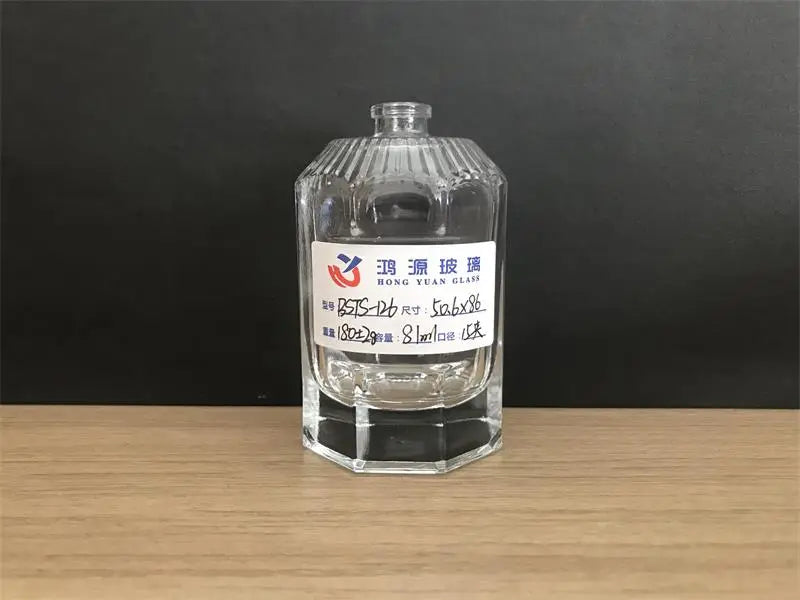 Multi-faceted cylindrical glass perfume bottle with vertical stripes on the shoulder