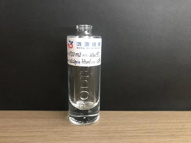 Cylindrical transparent glass perfume bottle with raised text